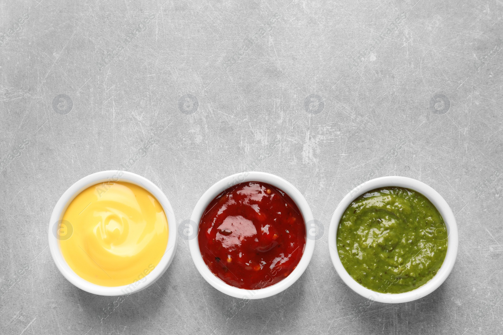 Photo of Set of different delicious sauces on grey table, top view. Space for text