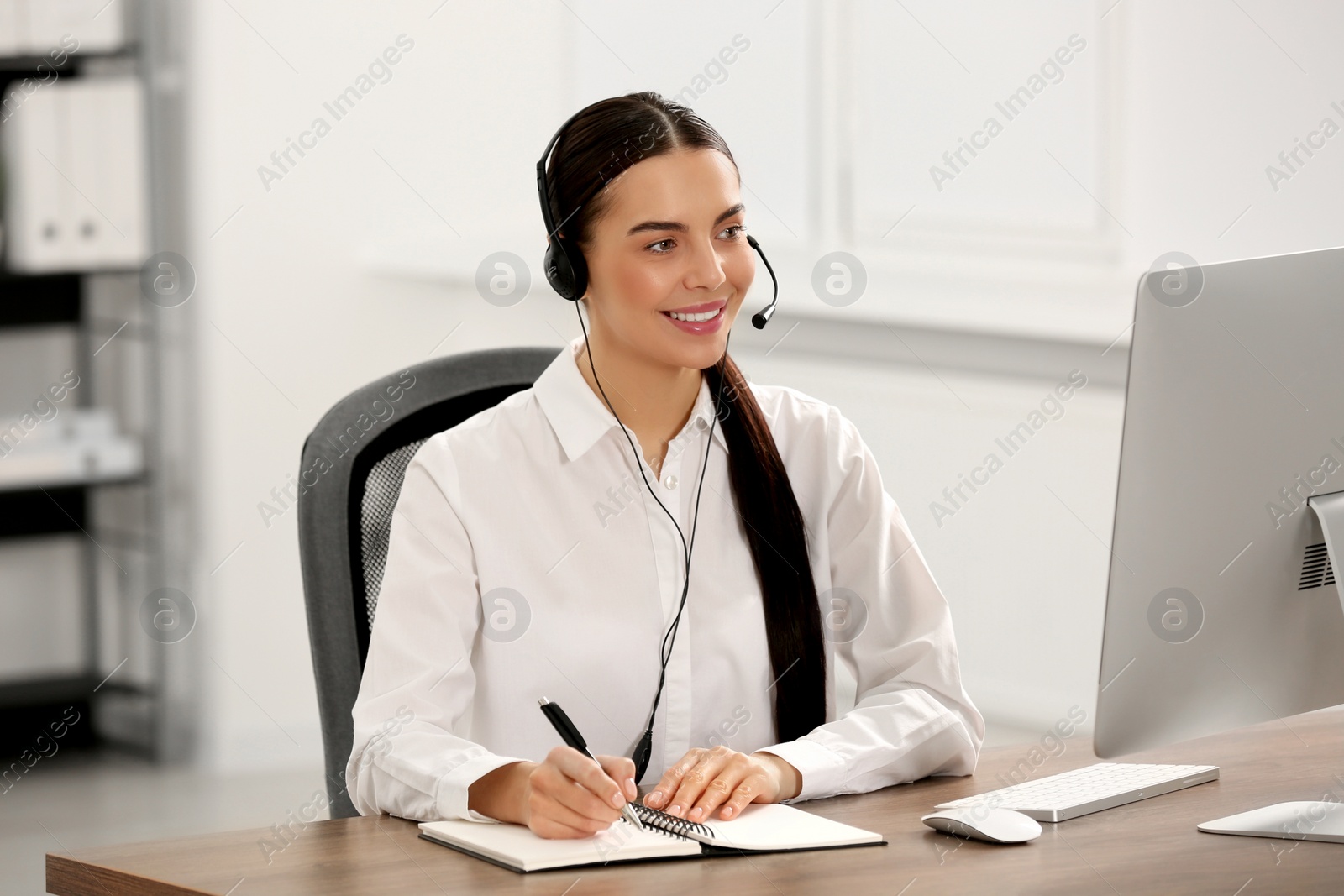 Photo of Hotline operator with headset and notebook working in office