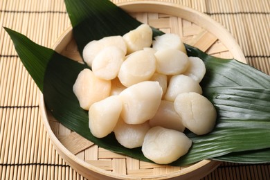 Photo of Fresh raw scallops in bowl on bamboo mat, closeup