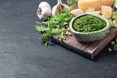 Photo of Bowl of tasty arugula pesto and ingredients on black table. Space for text