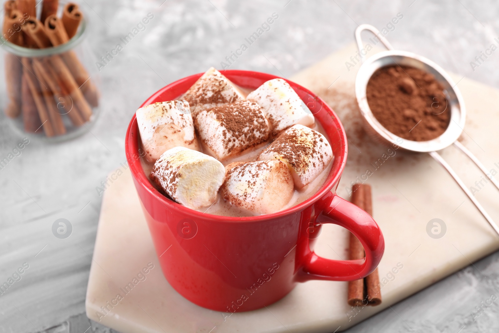 Photo of Cup of aromatic hot chocolate with marshmallows, cocoa powder and cinnamon sticks on table, closeup