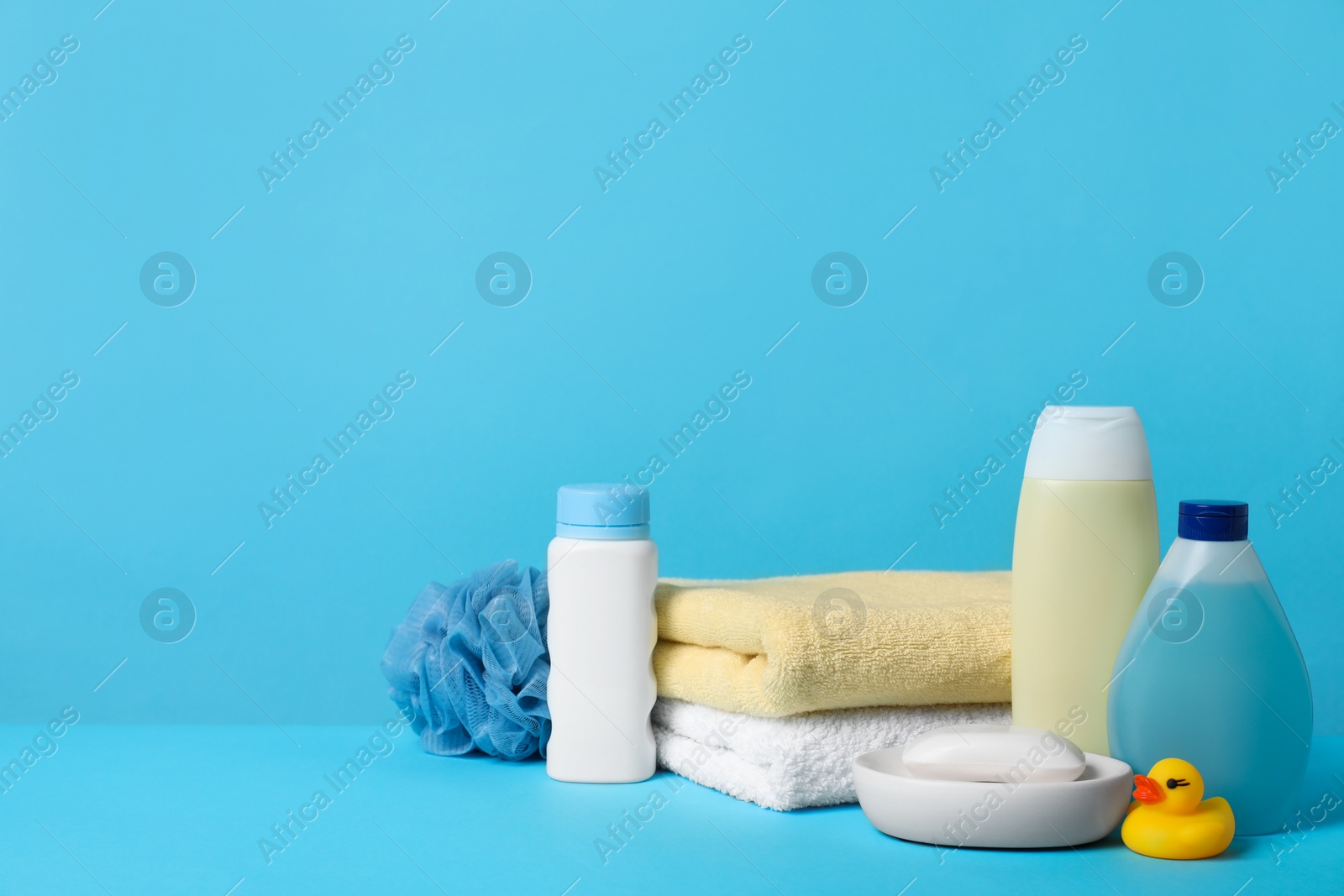 Photo of Baby cosmetic products, bath duck, sponge and towels on light blue background. Space for text