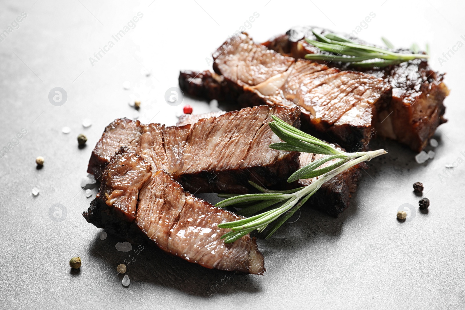 Photo of Pieces of delicious barbecued meat with rosemary on gray table