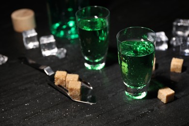 Photo of Absinthe in shot glasses, spoon, brown sugar and ice cubes on gray table, closeup. Alcoholic drink