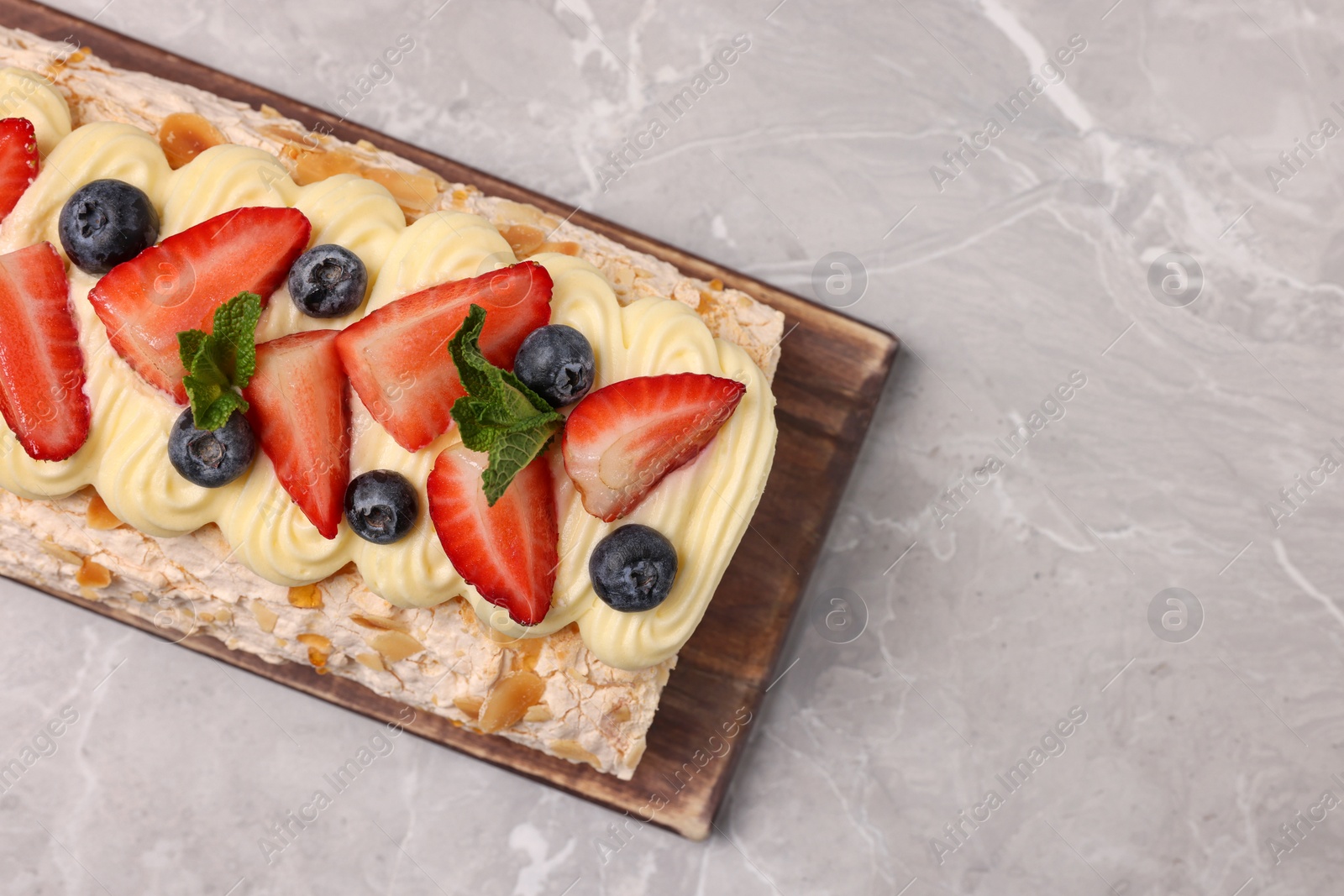 Photo of Tasty meringue roll with cream, strawberry, blueberry and mint on light grey marble table, top view. Space for text