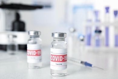 Photo of Vials with vaccine against Covid-19 and syringe on white table indoors