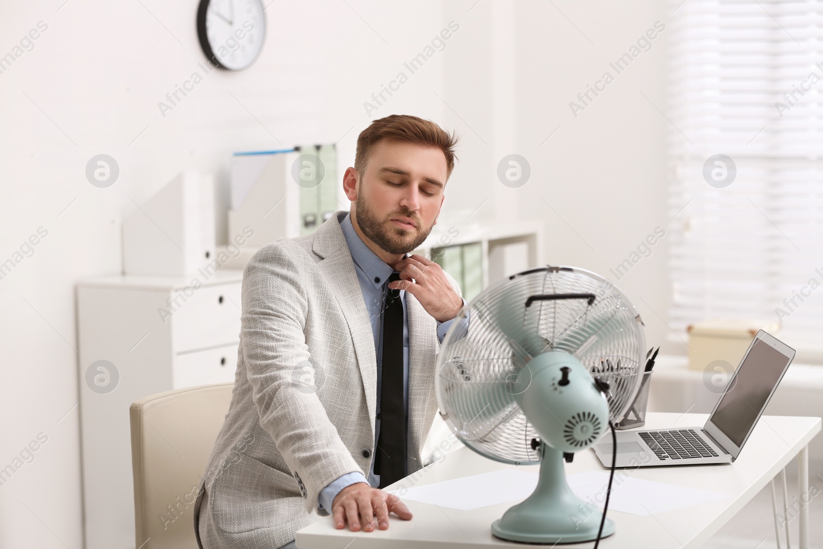 Photo of Man enjoying air flow from fan at workplace