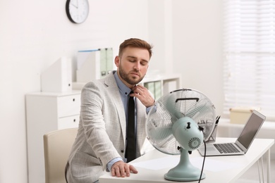 Man enjoying air flow from fan at workplace