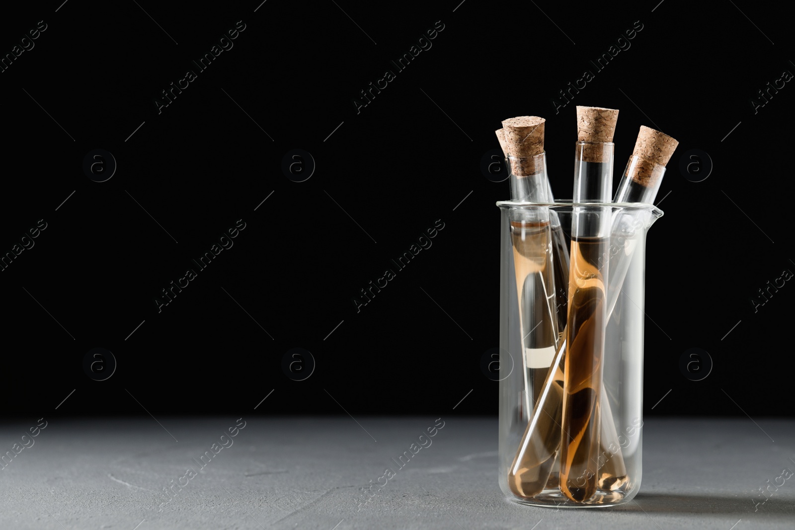 Photo of Test tubes with brown liquid on grey table. Space for text