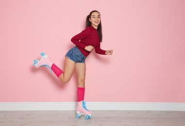 Young woman with roller skates near color wall