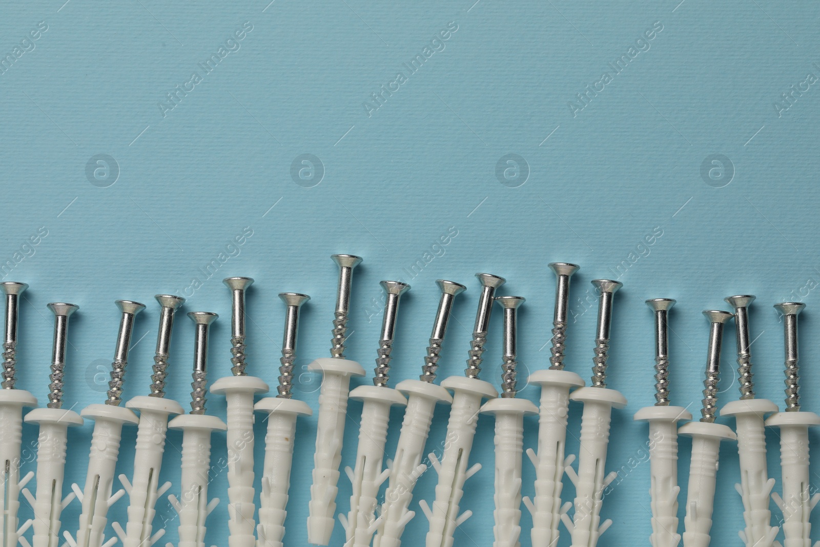 Photo of Many metal screws with white dowels on light blue background, flat lay. Space for text