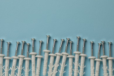 Many metal screws with white dowels on light blue background, flat lay. Space for text