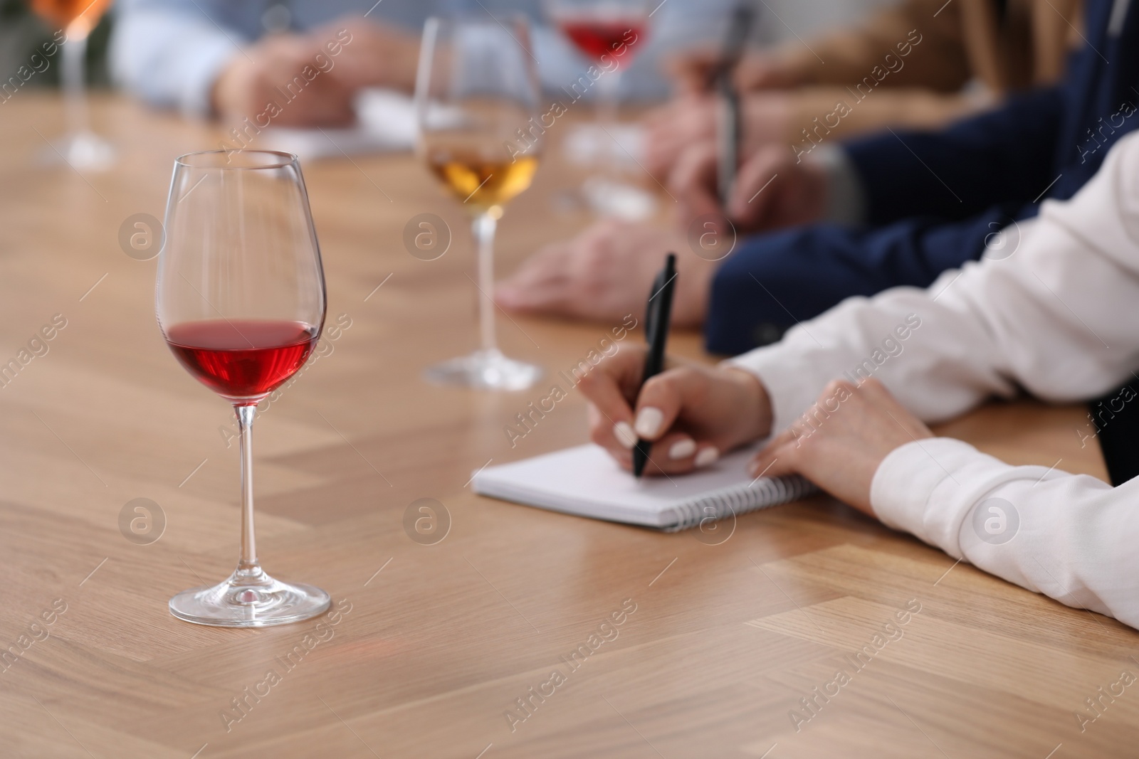 Photo of Sommeliers making notes during wine tasting at table indoors, closeup