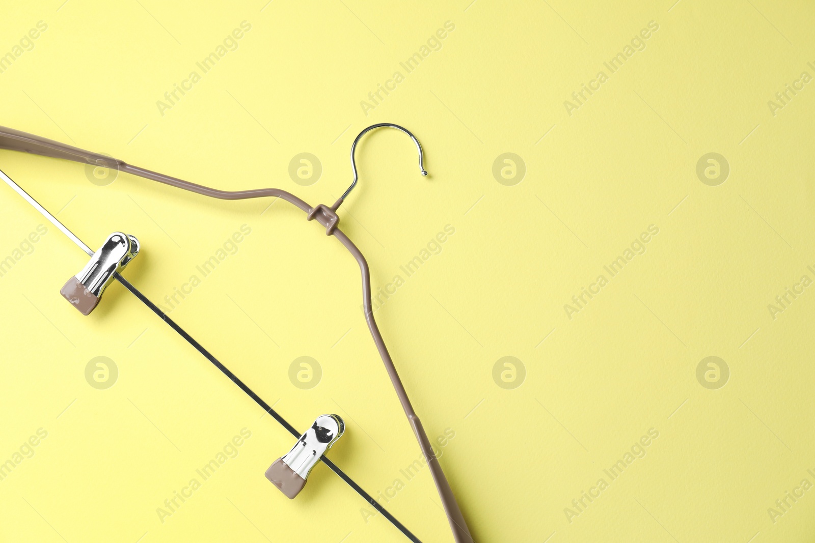 Photo of Empty hanger with clips on yellow background, top view. Space for text