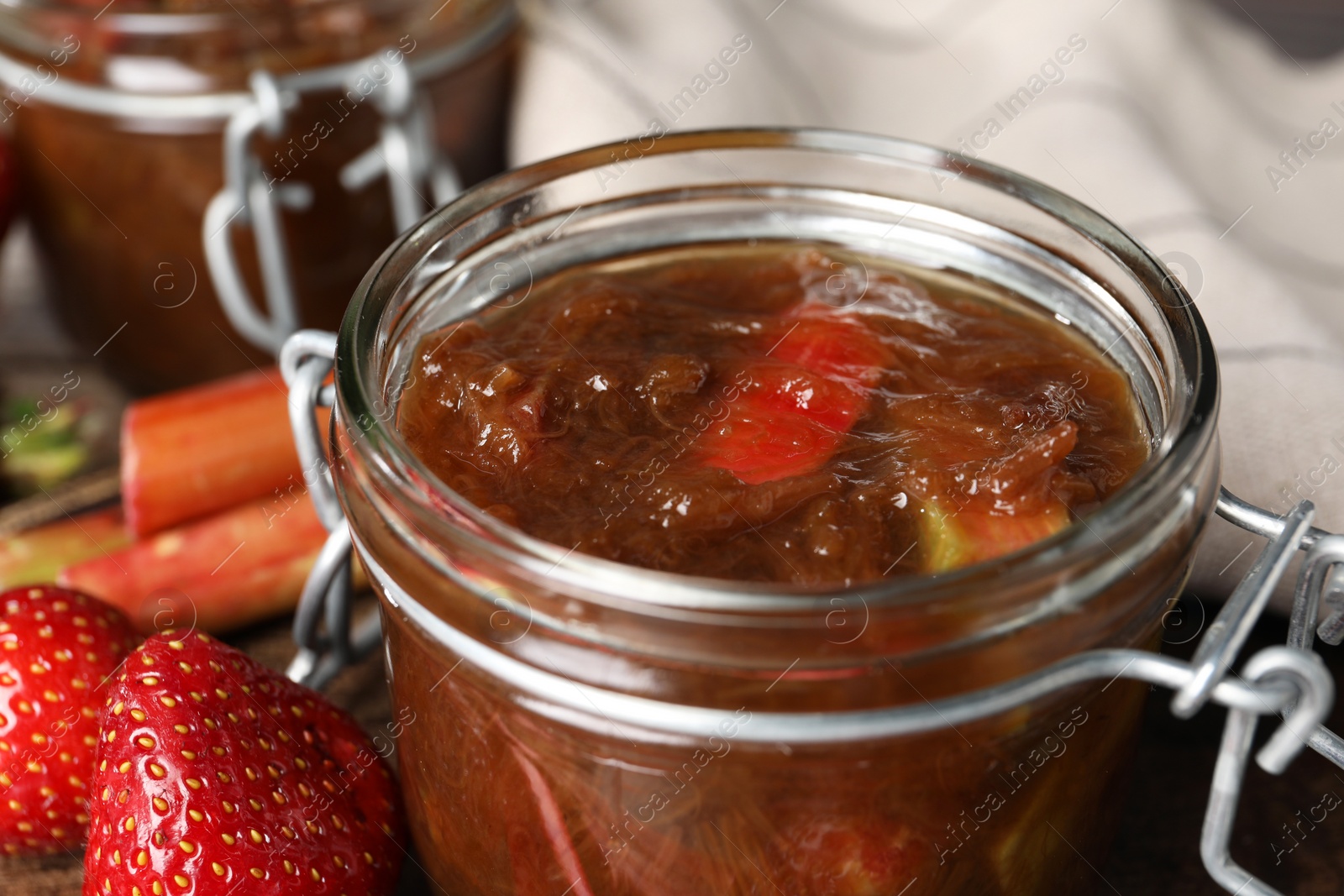 Photo of Jar of tasty rhubarb jam, fresh stems and strawberries on table, closeup