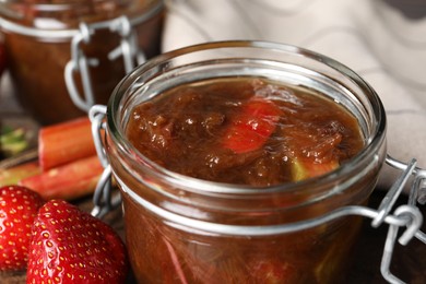 Photo of Jar of tasty rhubarb jam, fresh stems and strawberries on table, closeup