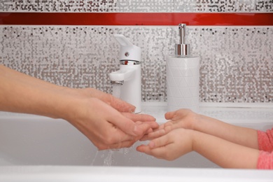 Photo of Mother and daughter washing hands in bathroom at home, closeup