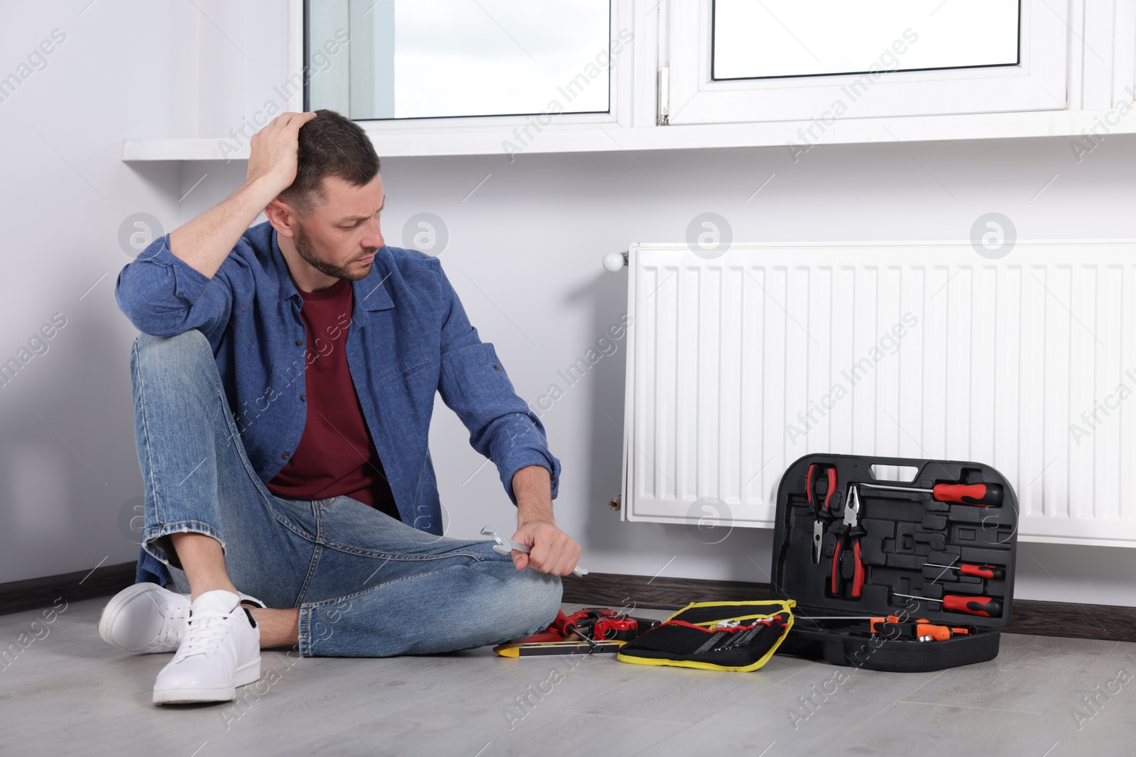 Photo of Man sitting on floor near box with tools indoors