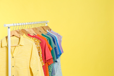 Photo of Bright clothes hanging on rack against yellow background, space for text. Rainbow colors