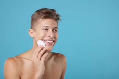 Photo of Handsome man cleaning face with cotton pad on light blue background, space for text