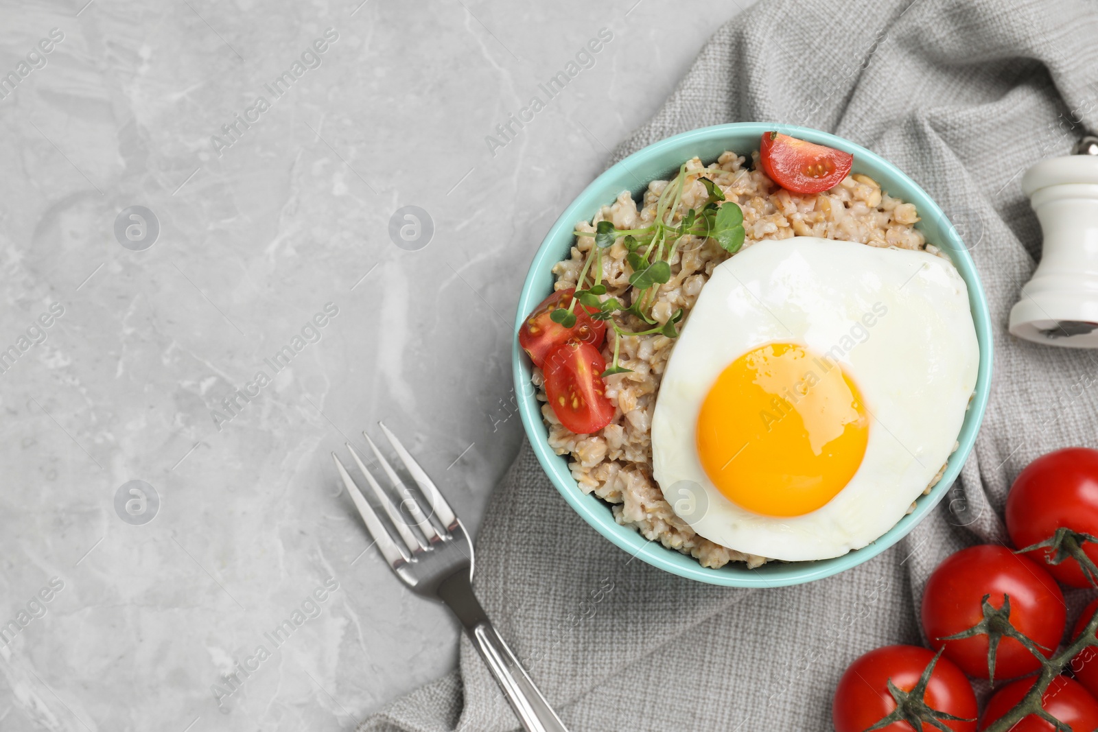 Photo of Tasty boiled oatmeal with fried egg, tomato and microgreens served on light grey table, flat lay. Space for text