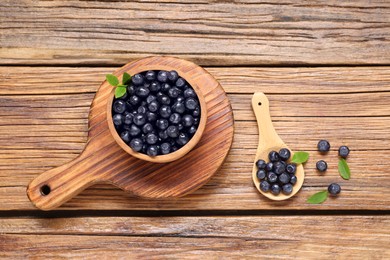 Photo of Ripe bilberries and leaves on wooden table, flat lay