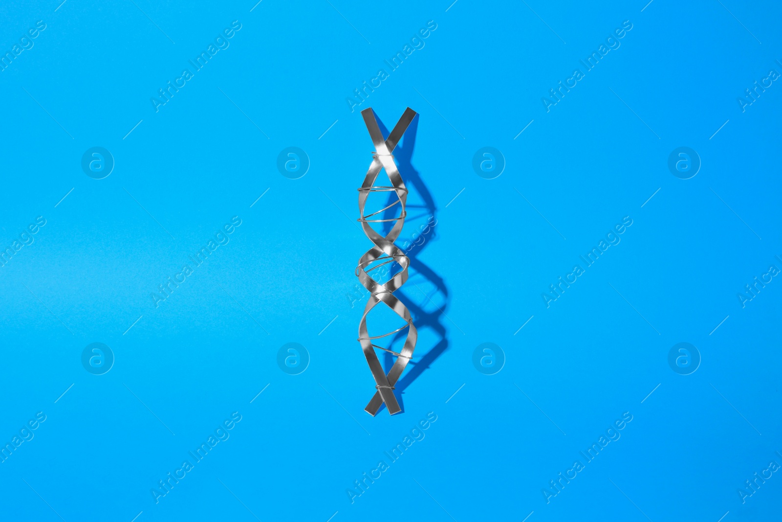 Photo of DNA molecular chain model made of metal on blue background, top view