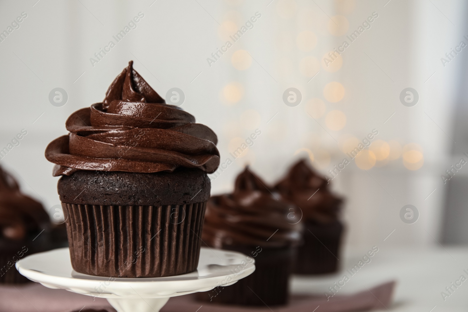 Photo of Dessert stand with delicious chocolate cupcake against blurred lights, closeup. Space for text