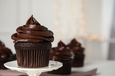 Dessert stand with delicious chocolate cupcake against blurred lights, closeup. Space for text