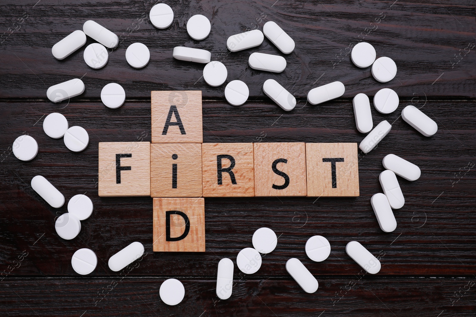 Photo of Words First Aid made of cubes and pills on black wooden table, flat lay