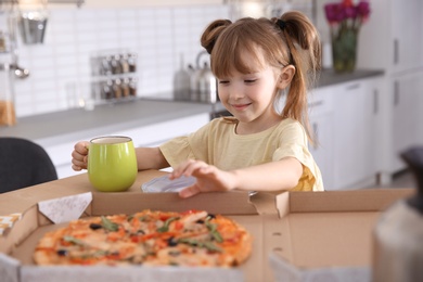 Photo of Cute little girl eating tasty pizza at home