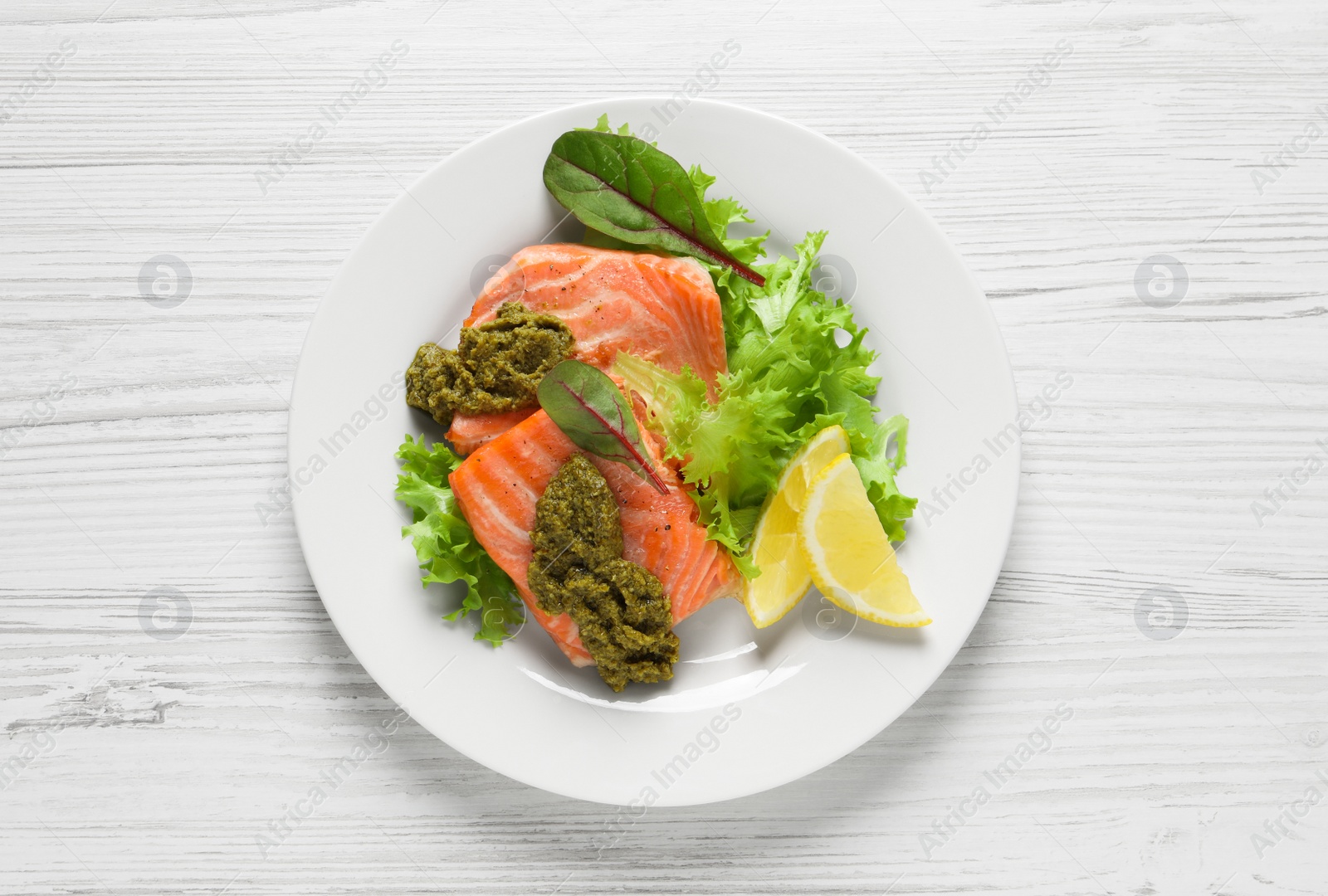 Photo of Tasty cooked salmon with pesto sauce on white wooden table, top view