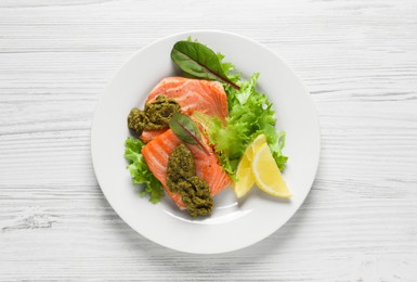 Photo of Tasty cooked salmon with pesto sauce on white wooden table, top view