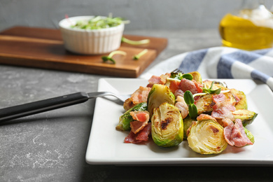 Photo of Delicious roasted Brussels sprouts with bacon served on grey table, closeup