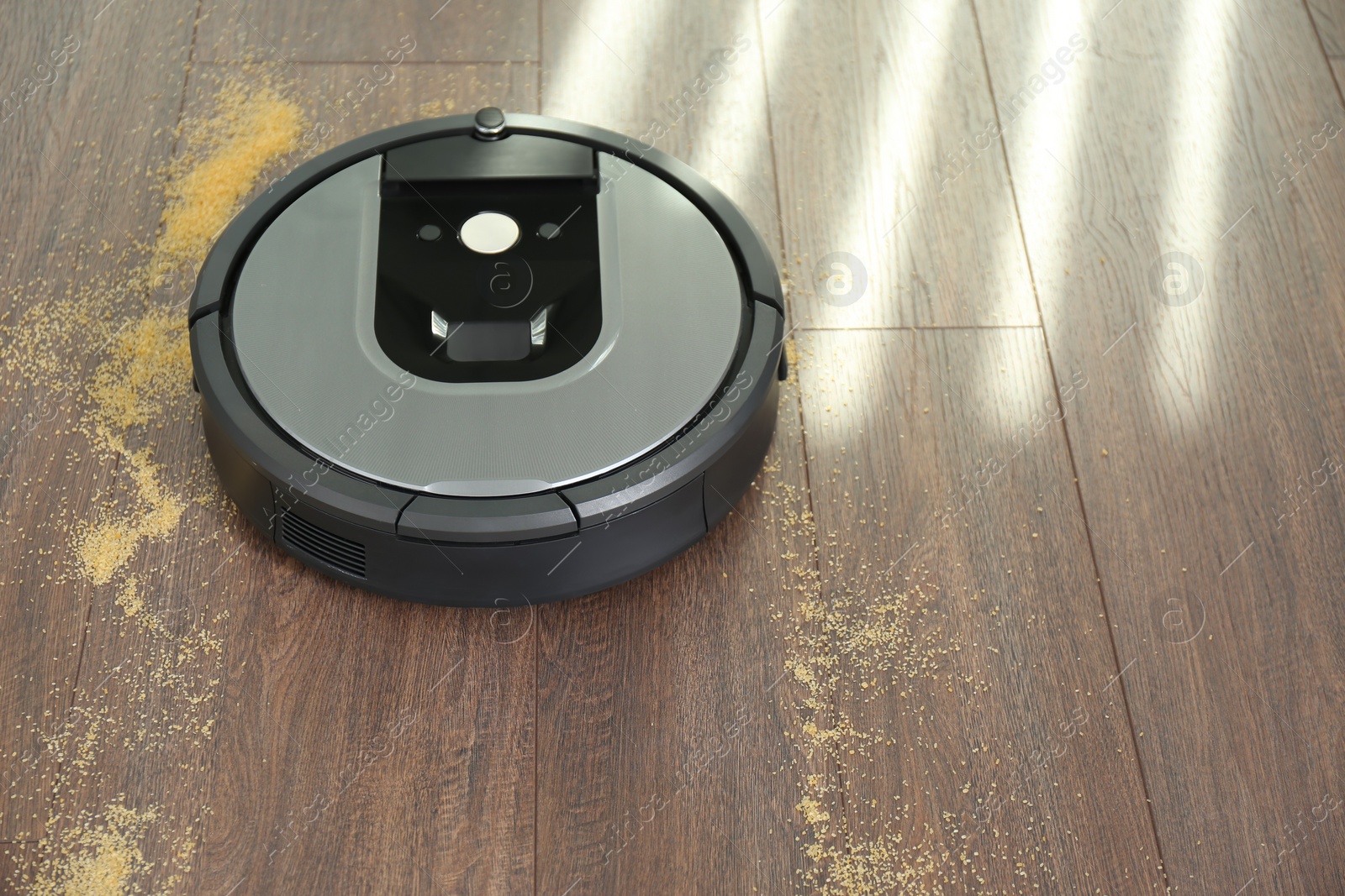 Photo of Modern robotic vacuum cleaner removing scattered groats from wooden floor. Space for text