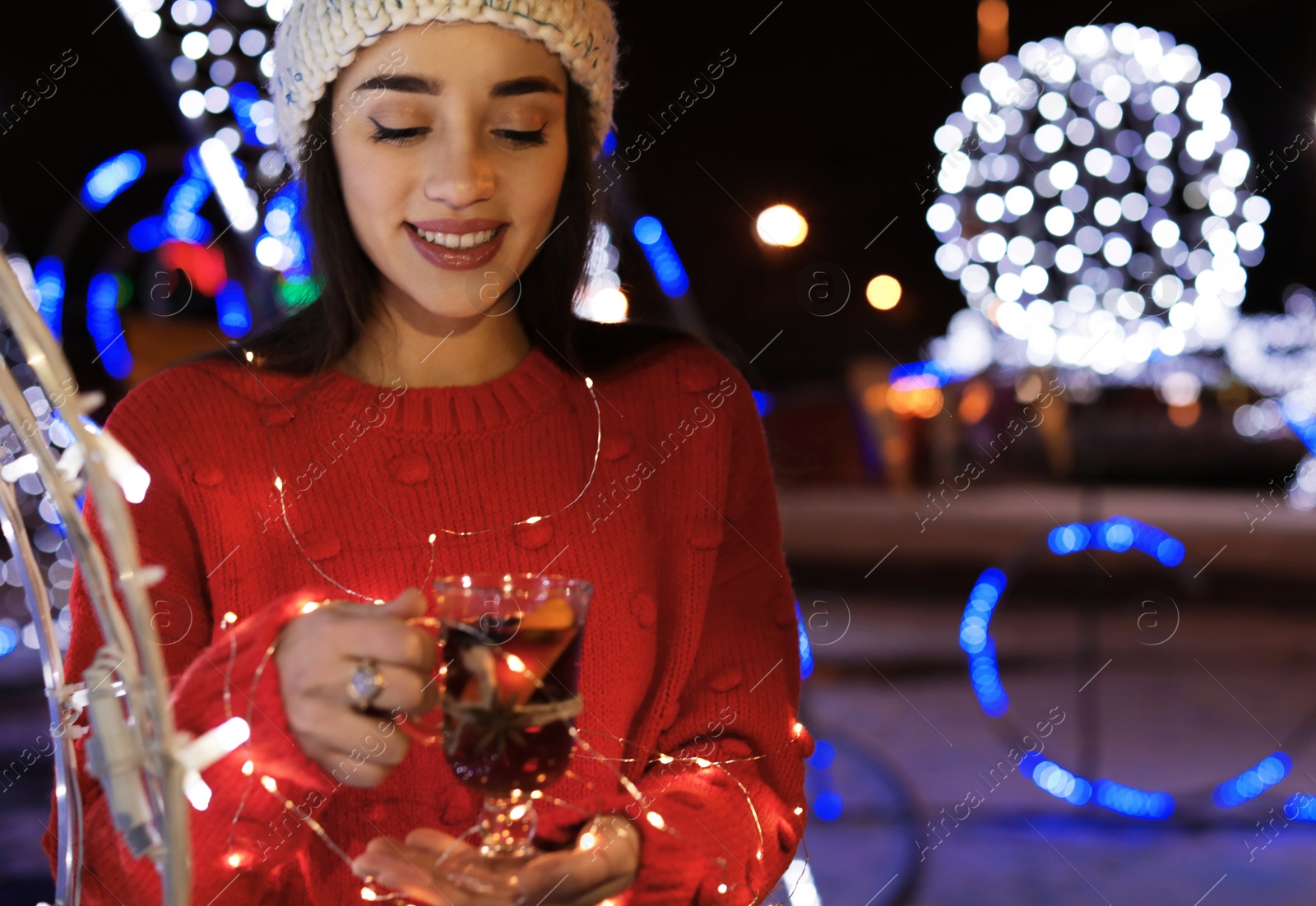 Photo of Woman with glass cup of mulled wine and garland at winter fair