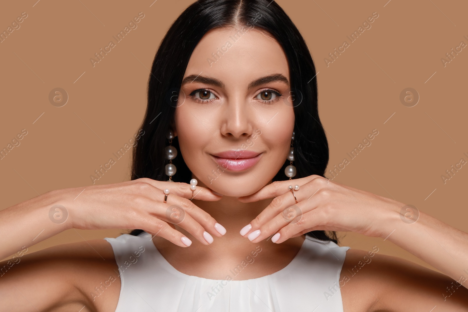 Photo of Young woman wearing elegant pearl jewelry on brown background