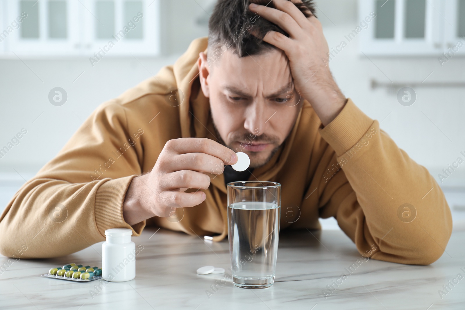 Photo of Man taking medicine for hangover at table in kitchen