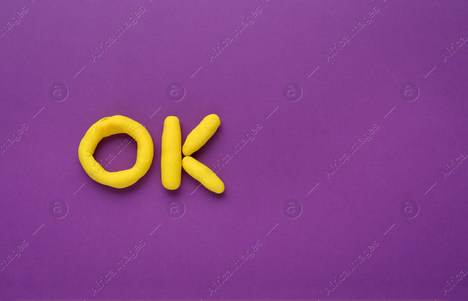 Photo of Word Ok made of yellow plasticine on purple background, top view. Space for text