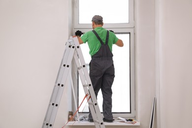 Worker in uniform installing double glazing window indoors, back view