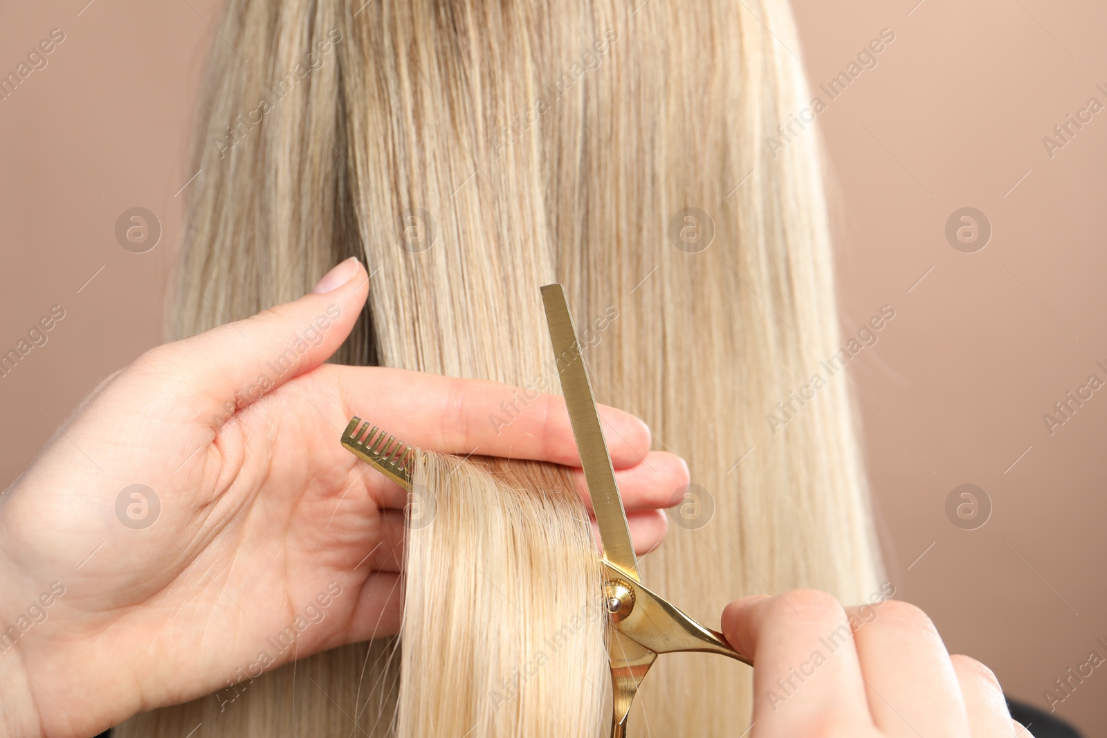 Photo of Hairdresser cutting client's hair with scissors on beige background, closeup