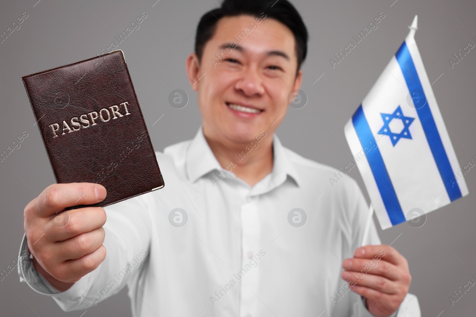 Photo of Immigration. Happy man with passport and flag of Israel on grey background, selective focus