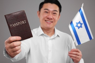 Photo of Immigration. Happy man with passport and flag of Israel on grey background, selective focus