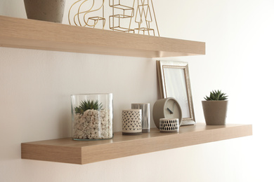 Wooden shelves with plants and decorative elements on light wall