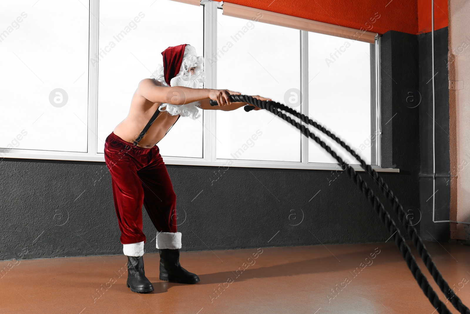 Photo of Young shirtless Santa Claus training with ropes in modern gym