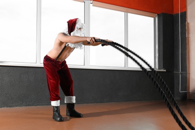 Young shirtless Santa Claus training with ropes in modern gym