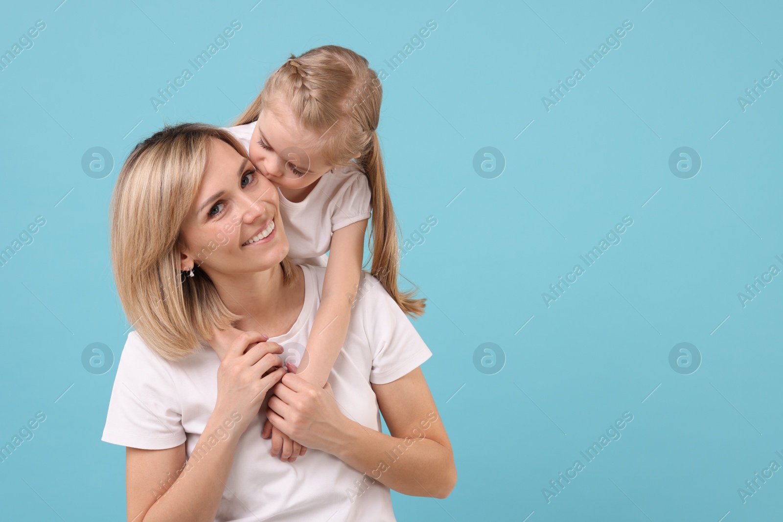 Photo of Daughter kissing her happy mother on light blue background. Space for text