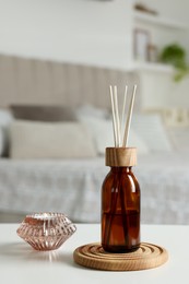 Photo of Aromatic reed air freshener and candle on white table in bedroom