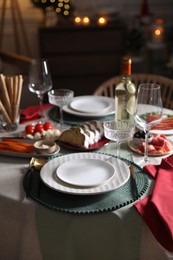 Photo of Christmas table setting with bottle of wine, appetizers and dishware indoors