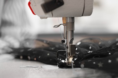 Photo of Sewing machine and black fabric with paillettes, closeup